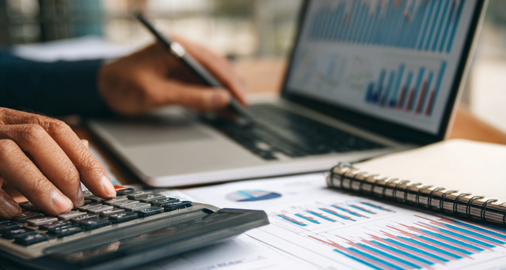 Close-up van een laptopscherm met vergelijkingsgrafieken voor hypotheekrentes en financiële diagrammen, handen die een rekenmachine gebruiken en aantekeningen maken,